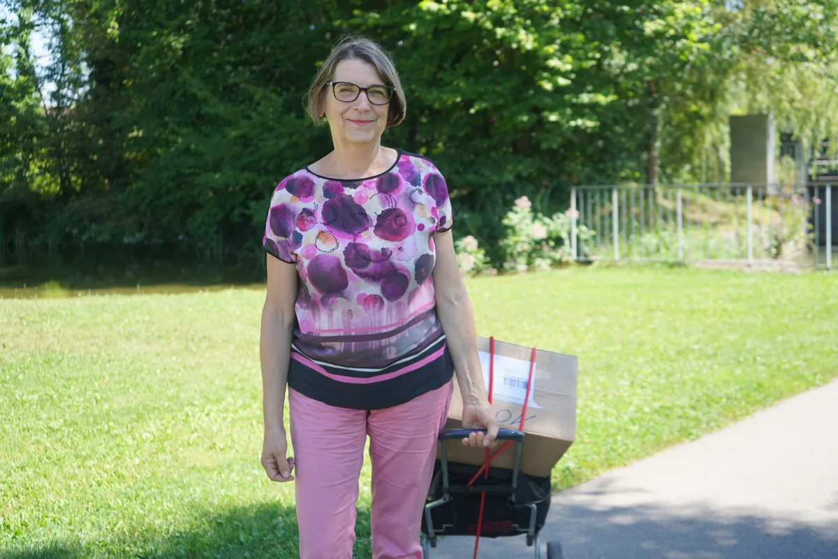 Die Autorin Eva-Maria Müller mit einem Postwägeli. Darauf sind Kartons.
